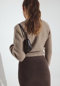 Pruun kootud kampsun ribadega äärega, kombineeritud tumepruuni karvase seelikuga. Õlal rippub väike must käekott.