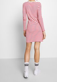 Abito a maniche lunghe a righe rosse e bianche con una silhouette aderente. Abbinato a sneakers bianche e calzini alla caviglia con righe nere.