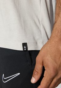 Lys grå bomulds t-shirt med en sort etiket med et logo, parret med sorte shorts der viser et hvidt Nike-logo.