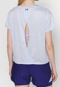 Vaaleansinen lyhythihainen urheilu(paita), jossa on avara kaula-aukko ja selän leikattu osa, paljastaen alla olevan kuvioidun urheiluliivin.