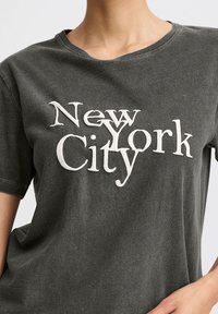 Dark gray short-sleeve t-shirt featuring white text reading "New York City" in various font styles. Soft fabric with a slightly worn texture.