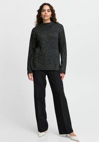 Czarny sweter o teksturowanej powierzchni z wysokim dekoltem i długimi rękawami, zestawiony z czarnymi spodniami o szerokich nogawkach i białymi szpilkami z ostro zakończonym noskiem.