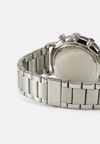 Montre en acier inoxydable argenté avec un bracelet à maillons lisses, un boîtier rond et deux poussoirs sur le côté droit. Logo de la marque gravé sur le fermoir.