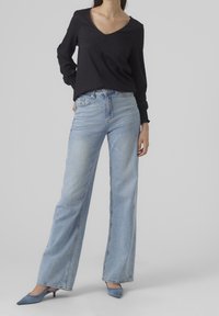 Top nero a maniche lunghe con scollatura a V abbinato a jeans a gamba larga azzurri e décolleté blu a punta. Tessuto morbido con polsini arricciati sulle maniche.