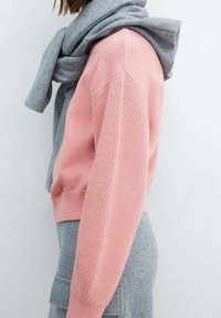 Vaaleanpunainen neulepaita, jossa on teksturoidut olkapään yksityiskohdat, yhdistetty vaaleanharmaaseen huiviin, joka on laskostettu kaulan ympärille, sivuprofiili näkyvissä.