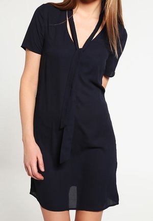 Abito blu navy a maniche corte con profondo scollo a V e dettaglio con fiocco, realizzato in tessuto leggero con una superficie liscia.