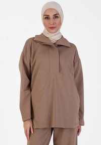 Bruine lange mouw top met een polo kraag en een rechthoekige knopenrij, gemaakt van zachte stof met een gladde textuur.