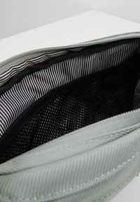 Sac en tissu vert clair avec une ouverture zippée, doté d'une doublure en maille noire et d'un motif intérieur rayé en blanc et noir.