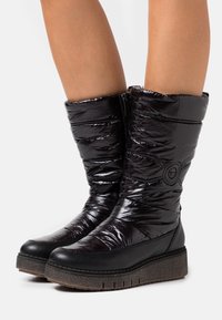 Schwarze, gepolsterte Winterstiefel mit glänzender Oberfläche, Knöchelhöhe, ausgestattet mit einem Reißverschluss und einer strukturierten Keilsohle. Abgerundet mit einem Logodetail.