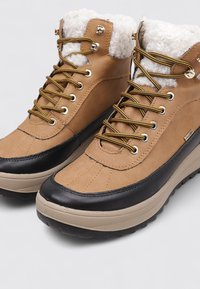 Braune und schwarze Knöchelboots mit Kunstfellfutter, strukturiertem Leder und Gummisohle, ausgestattet mit goldfarbenen Ösen und Schnürsenkeln.