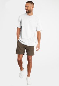 Hvid kortærmet t-shirt parret med olivengrønne shorts og hvide sneakers. Casual fit med rund hals og minimale design detaljer.