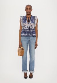 Top con estampado floral y mangas abullonadas, con detalles de lazo y acentos en azul. Combinado con jeans rectos de un azul claro y un bolso de mimbre.