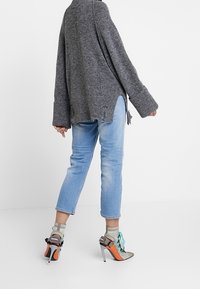 Grauer übergroßer Pullover mit gerippten Bündchen, kombiniert mit hellblauen Jeans und High Heels mit Netzstruktur und bunten Akzenten.