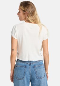 Top bianco a maniche corte in tessuto ribbed con scollatura tonda, abbinato a jeans in denim blu a vita alta con tasche posteriori e dettagli di cucitura.