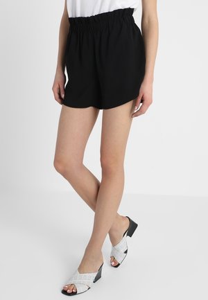Black, elastic-waist shorts with a loose fit, paired with silver, open-toe block-heel sandals featuring a textured pattern.