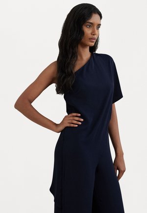 Marineblå ensidig jumpsuit med avslappet passform, glatt stoff og bred benløsning. Har subtil drapering på siden for ekstra detaljer.