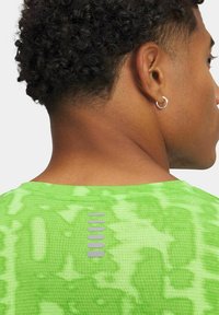 T-shirt verde brillante con un motivo testurizzato. Presenta un dettaglio riflettente sulla schiena e un design a girocollo.