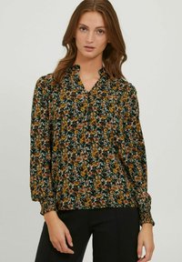 Bluse mit floralem Muster und V-Ausschnitt, auf einem dunkelgrünen Hintergrund mit einer Mischung aus gelben und braunen Blumen. Lange Ärmel mit gerafften Manschetten.
