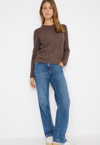 Brauner gerippter Strickpullover mit langen Ärmeln, kombiniert mit hellblauen Schlagjeans. Die Jeans haben eine ausgeblichene Textur und ein klassisches Fünf-Taschen-Design.
