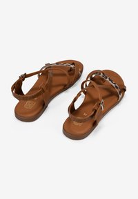 Sandalias marrones con correas cruzadas y acentos de estampado animal, con un tacón texturizado y hebilla ajustable. Suela suave y plana.