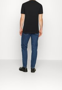 Sort kortærmet t-shirt, ensfarvet, parret med blå denim jeans. Sorte ankelstøvler synlige. Enkel, afslappet pasform.