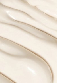 Cremige, ivoryfarbene Lotion mit glatter, gewellter Textur und glänzendem Finish, die subtile Variationen in Dicke und Glanz zeigt.