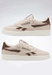 Paire de baskets basses Reebok beige et marron avec semelles blanches, design à lacets, et logo Reebok sur le côté et la languette.