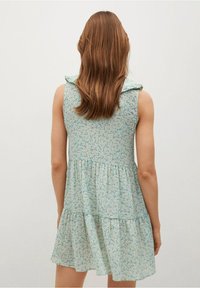 Vaalean sininen kukallinen mekko, jossa on frillaolkaimet, kerroksellinen hame ja teksturoitu kuvio. Olkaimeton malli, takanäkymä näkyvissä.