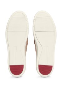 Semelle extérieure de chaussures Tommy Hilfiger beige avec semelle blanche texturée et patchs en caoutchouc rouges au talon, vue par dessous sur fond blanc.