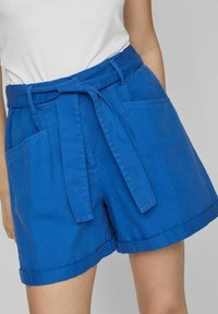 Blue, high-waisted shorts made of denim with a tie belt, featuring two side pockets and rolled hems. Smooth texture, casual design.