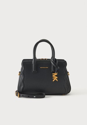 Czarna torebka Michael Kors z falistymi brzegami, podwójnymi uchwytami, złotym breloczkiem MK i odpinanym paskiem na ramię na białym tle.
