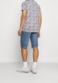 Grå t-shirt med palmträdsmönster, blå denimshorts, vita strumpor, ljusa sneakers. Avslappnad outfit sedd bakifrån.