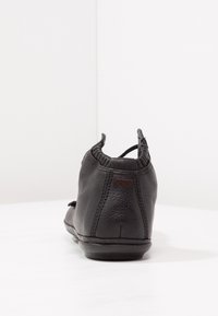Chaussure décontractée en cuir noir vue de dos avec des coutures visibles et une petite languette au niveau du col du talon.