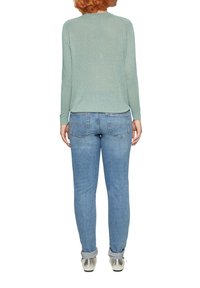 Jasnozielona bluzka z długim rękawem o teksturowanym, połyskującym wykończeniu, zestawiona z dopasowanymi, jasnoniebieskimi dżinsami i srebrnymi butami.