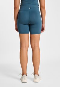 Tealfärgade sportshorts med hög midja och slät textur, som har ett diskret mönster på midjebandet och en logotypdetalj på baksidan.