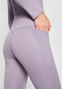 Levandų spalvos užpildytos legging'os su šonine kišenėle, be siūlių dizainas ir lygus paviršius. Matoma siuvimo detalė palei siūles.