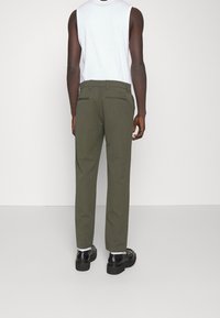 Olivgrüne Hosen mit geradem Schnitt, ausgestattet mit Seiten- und Gesäßtaschen. Kombiniert mit einem weißen ärmellosen Oberteil und schwarzen Schuhen.