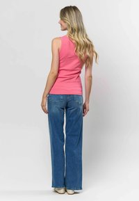 Rozā ribota tanka ar pieguļošu dizainu, apvienota ar gaiši ziliem platajiem džinsiem, valkāta ar krēmkrāsas apaviem. Aizmugures skats.