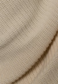 Gebreide stof in lichtbeige, met een ribbelstructuur en afwisselende diagonale en horizontale lijnen. Zachte, dikke garen samenstelling.