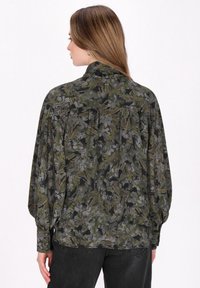 Bluză cu mâneci lungi, cu un model floral verde închis și negru, dintr-un material moale, cu guler înalt și detalii pliate la spate.