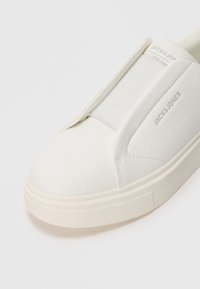 White slip-on sneaker with textured faux leather upper. Elastic side panel and rubber sole with subtle traction detail. Jack & Jones branding visible.