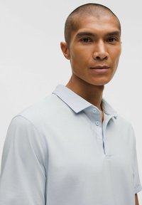 Jasnoniebieska koszulka polo wykonana z gładkiego materiału, z kołnierzykiem, dwoma guzikami i krótkimi rękawami. Minimalistyczny design bez widocznych wzorów.