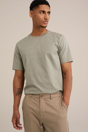 Lys grå bomulds t-shirt med rund halsudskæring og korte ærmer, kombineret med beige bukser. T-shirten har en glat tekstur.