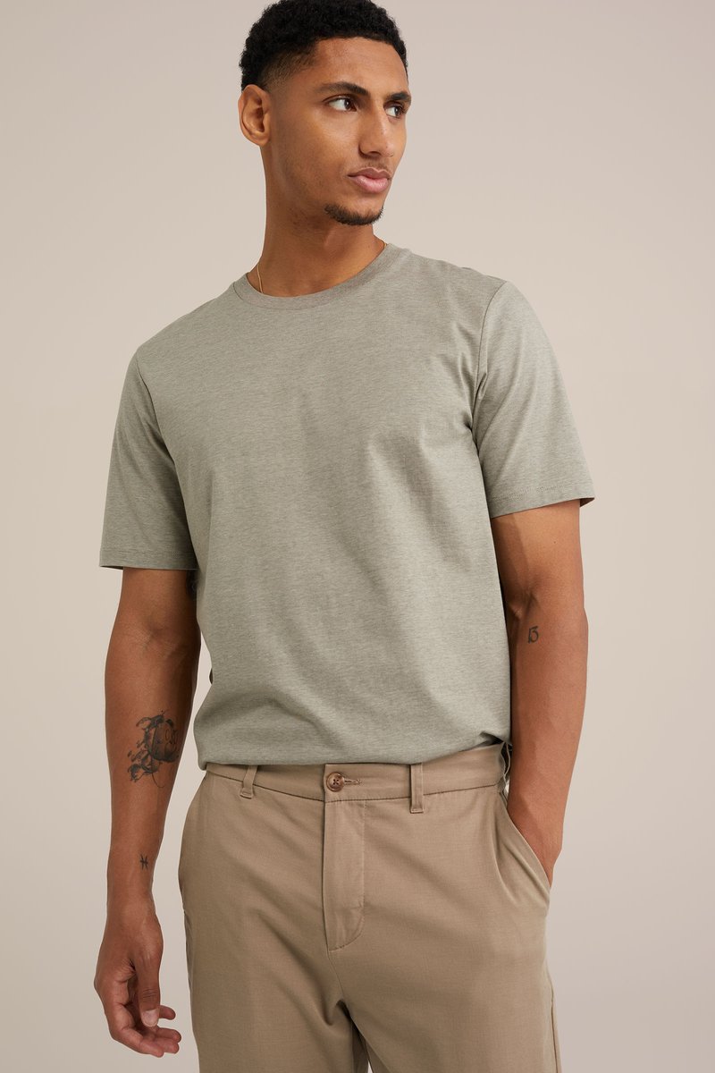 Gaiši pelēks kokvilnas T-krekls ar apaļu kakla izgriezumu un īsām piedurknēm, kopā ar bežām biksēm. T-kreklam ir gluda tekstūra.