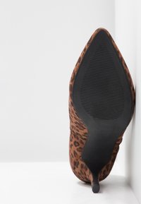 Scarpa con tacco alto a punta, con tomaia in suede maculato marrone e suola in gomma nera con scanalature per la trazione.