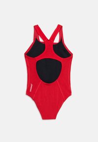 Κόκκινο ολόσωμο μαγιό με τιράντες racerback, μαύρη εσωτερική επένδυση και ανοιχτό άνοιγμα στην πλάτη, με ετικέτα "ENDURANCE+" στην αριστερή πλευρά.