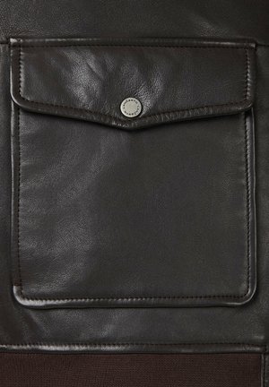 Ciemnobrązowa skórzana kieszonka z klapą i srebrnym zapięciem na zatrzask, z widocznym szwem i gładką teksturą na ciemniejszym tle.