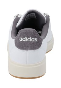 Vita Adidas-sneakers med en grå mocka hältab, strukturerad tyg och ljus sula. Har en rund tå och en vadderad krage.