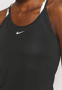 Svart atletisk linne gjort av stretchigt tyg, med en elegant design, racerback-stil, och en liten vit Nike-logotyp på bröstet.