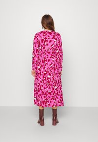Long pink dress with a bold red and white animal print, featuring long sleeves and a belted waist. Paired with brown block-heeled boots.